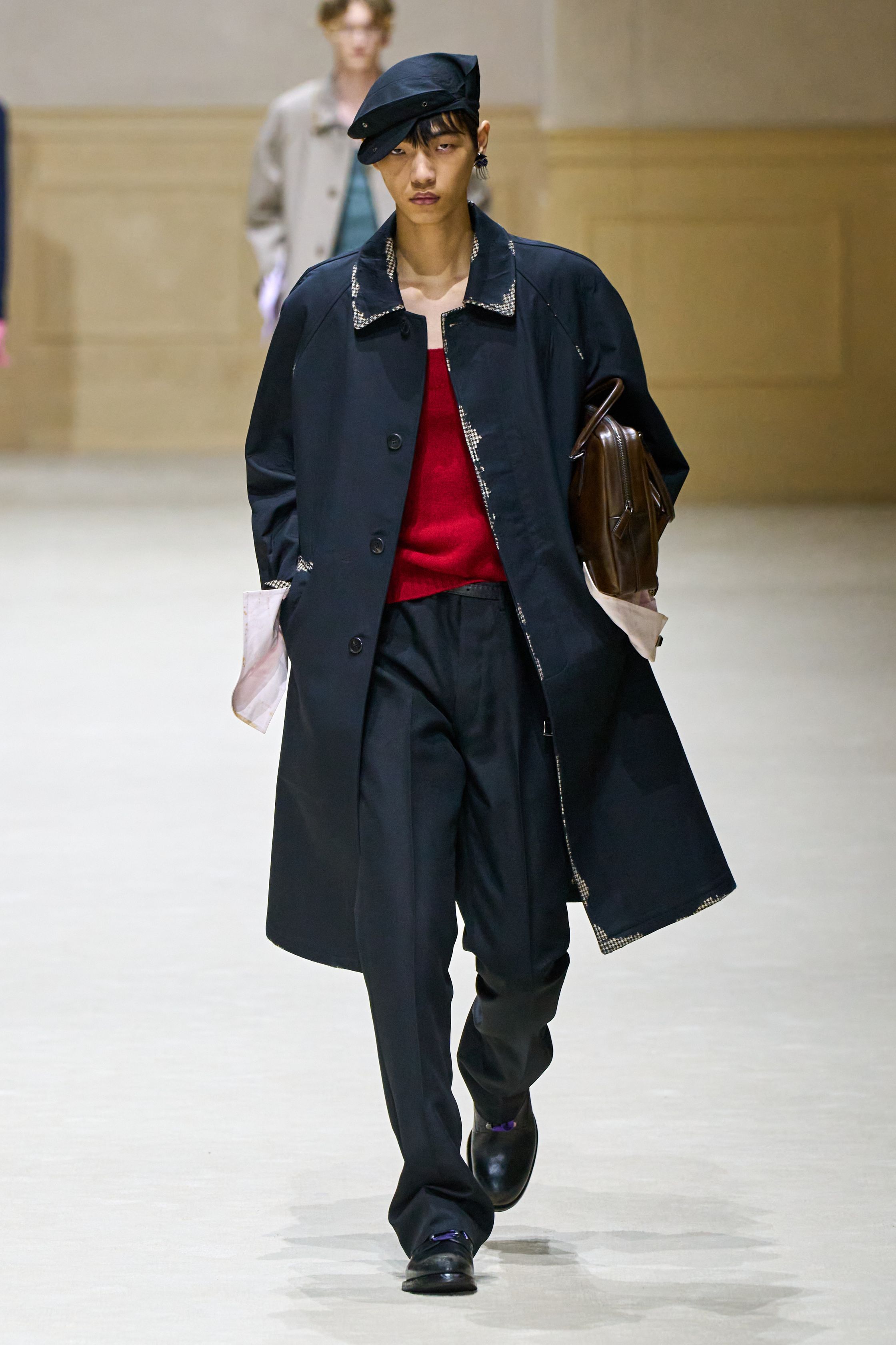 Prada 2026秋冬继续以“制服感”为切入口，重构男性权力与脆弱性的关系。修身西装、直筒大衣与功能性外套在高度理性的廓形中出现，却通过红色针织、围巾与内搭打破秩序。系列在严肃与松动之间反复摇摆，呈现一种当代男性在社会角色与个体情绪之间的张力。这是Prada一贯的冷静叙事，也是其思想性持续领先的关键简-顽石频道趋势研究